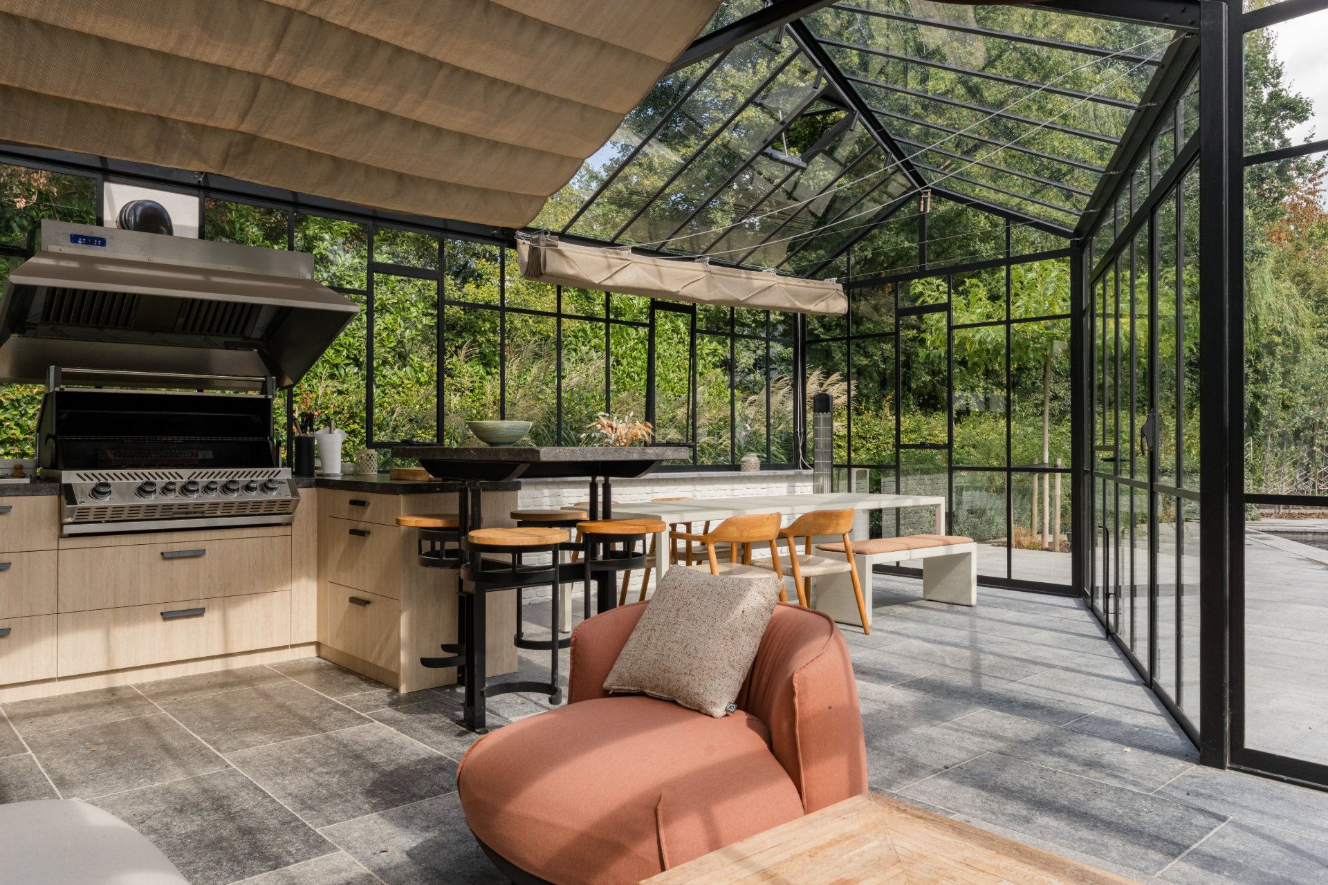Stalen orangerie met glazen dak, buitenkeuken en zithoek met zicht op de tuin