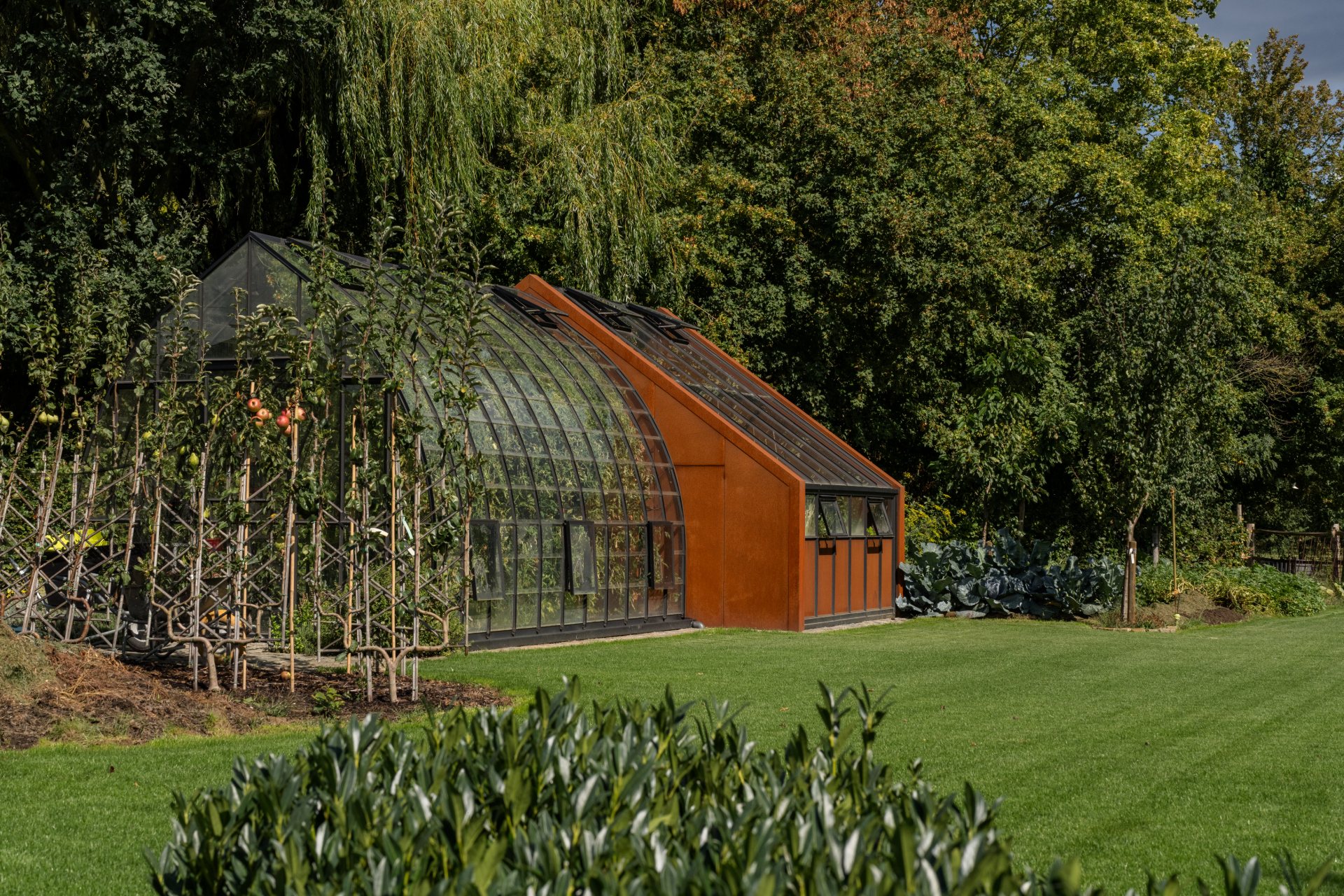 Tuinserre in zwart staal en glas met gebogen dak tussen de beplanting